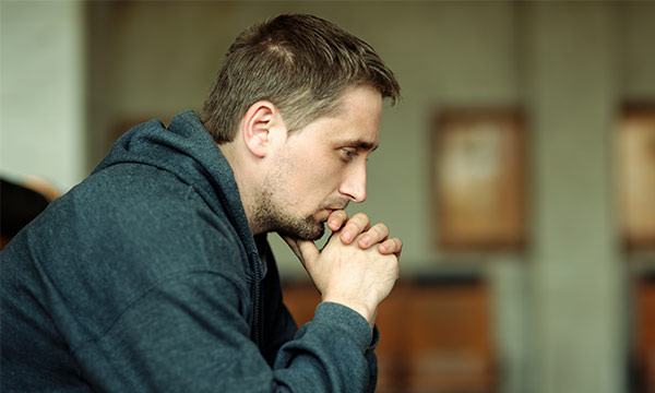 Mann mit Kapuzenpullover mit verschränkten Händen, wirkt nachdenklich